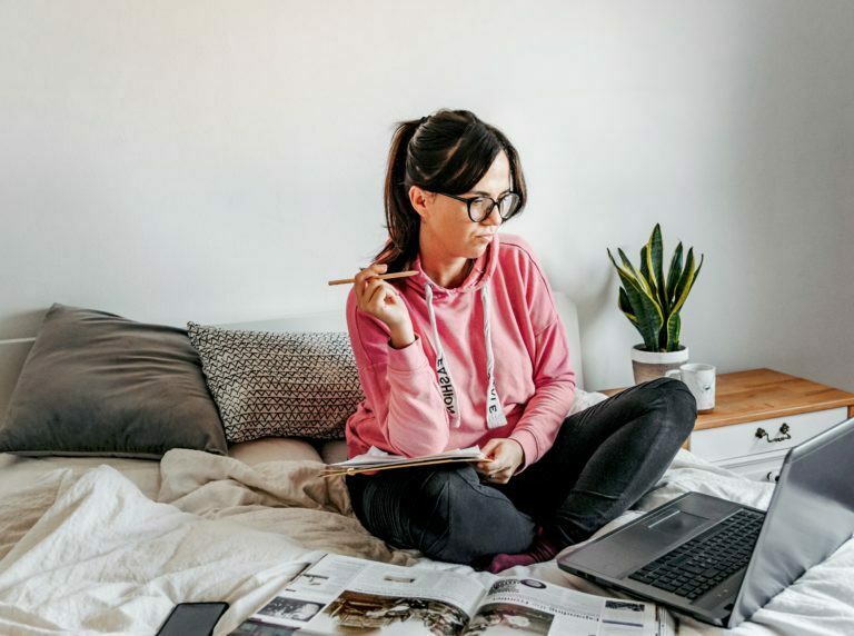 a woman sitting on a bed with a laptop and papers