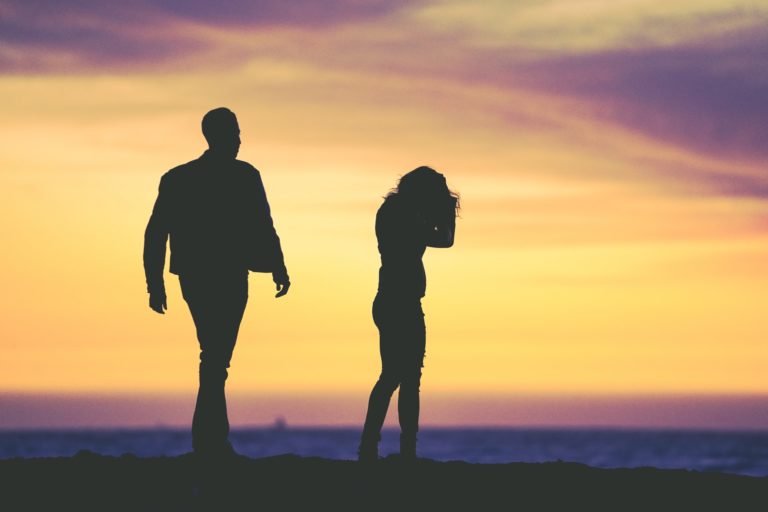 a man and woman walking on a beach at sunset